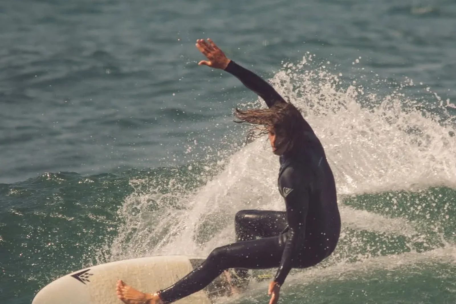 Surfista a rasgar a onda com spray, fotografado da areia pela BAD SURF PHOTO
